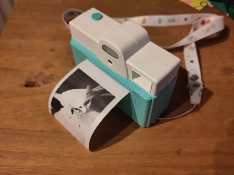 A photo of a children’s digital camera that prints photos to rolls of thermal receipt paper. It has printed a black and white photo of my cat Easóg.