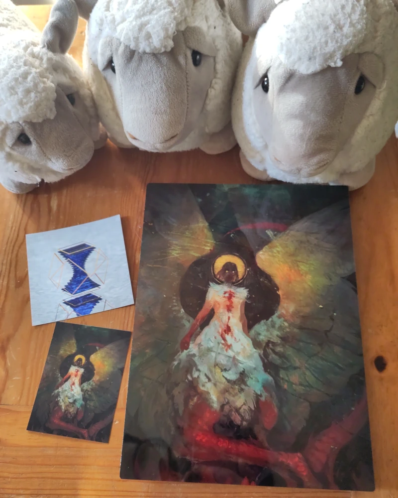 Large and small prints of a digital painting of Falin Touden from Dungeon Meshi in her monstrous form. Ellie used it as the avatar for her Discord ellie_online. There is also a small print of a floating crystal in a small golden cage. Three plush sheep toys are looking at the prints.