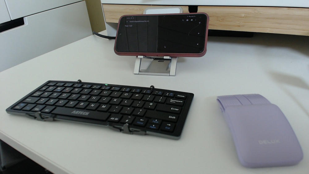 My phone on a little stand with a mini keyboard and mouse, making a tiny mobile desktop computer setup.