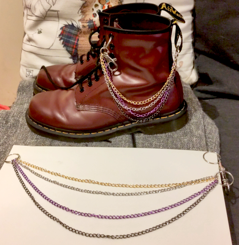 Two sets of chains in gold, silver, purple, and black. A shorter set hanging from a pair of Doc. Martens and a longer one on its own.